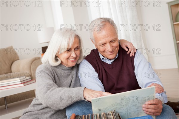 Smiling senior couple looking at vinyl's in living room. Photo : Rob Lewine