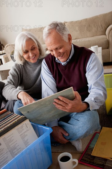 Smiling senior couple looking at vinyl's in living room. Photo : Rob Lewine