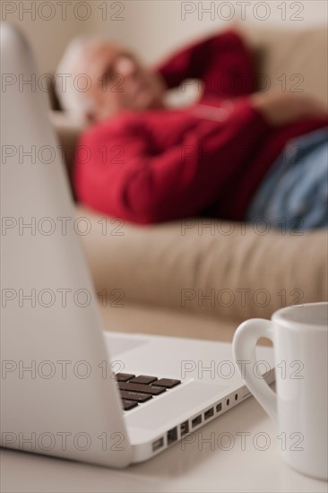 Senior man sleeping on sofa, laptop and mug in foreground. Photo : Rob Lewine