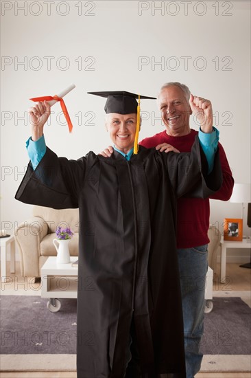 Senior woman wearing graduation gown, happy man in background. Photo : Rob Lewine