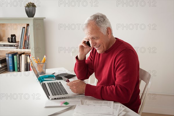 Senior man holding credit card and talking via mobile. Photo : Rob Lewine