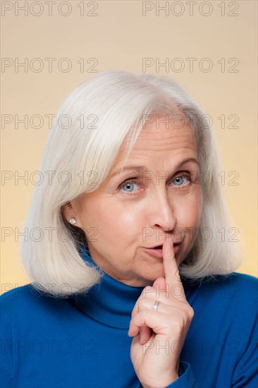 Studio shot of senior woman with finger on her lips. Photo : Rob Lewine