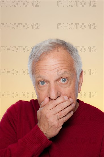 Studio shot of senior man covering lips. Photo : Rob Lewine