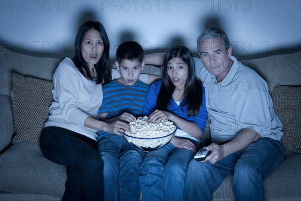 Family sitting on sofa and watching television. Photo : Rob Lewine