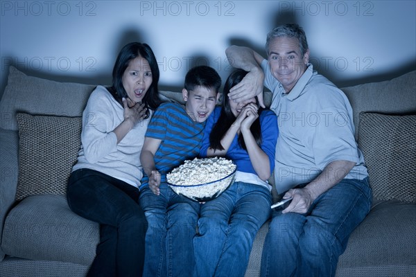 Family sitting on sofa and watching television. Photo : Rob Lewine