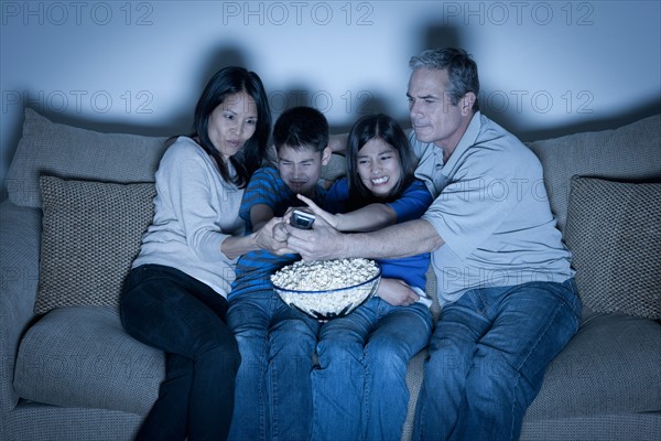 Family sitting on sofa and watching television. Photo : Rob Lewine