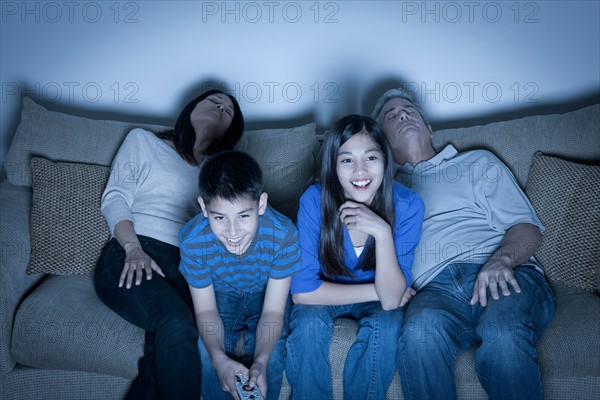 Family sitting on sofa and watching television. Photo : Rob Lewine