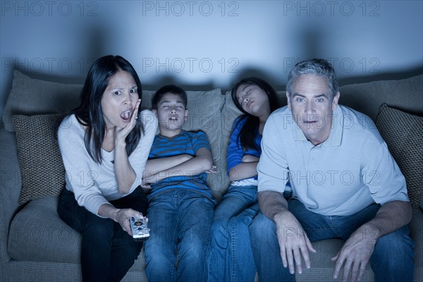 Family sitting on sofa and watching television. Photo : Rob Lewine