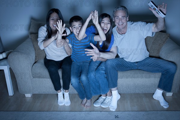 Family sitting on sofa and watching television. Photo : Rob Lewine