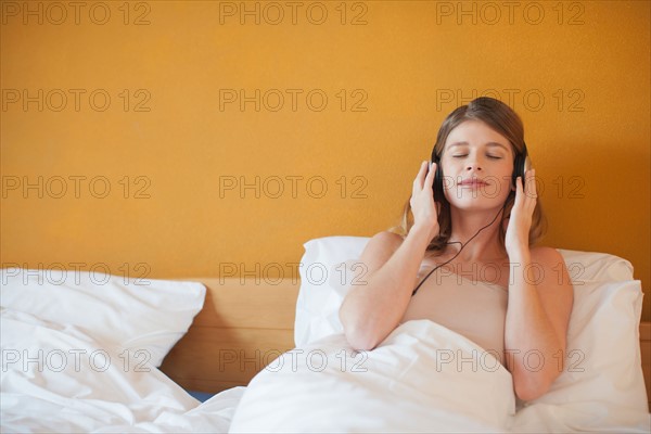 Young woman listening to music in bed. Photo : Mark de Leeuw