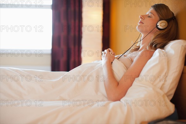 Young pregnant woman listening to music in bed. Photo : Mark de Leeuw