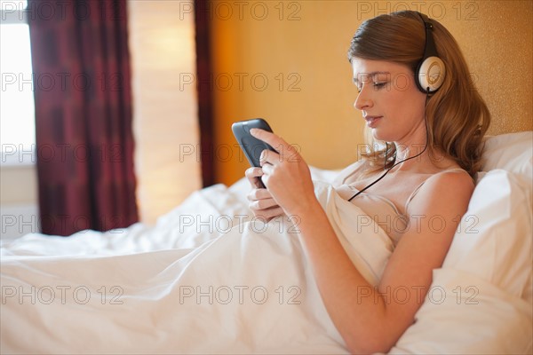 Young pregnant woman listening to music in bed. Photo : Mark de Leeuw