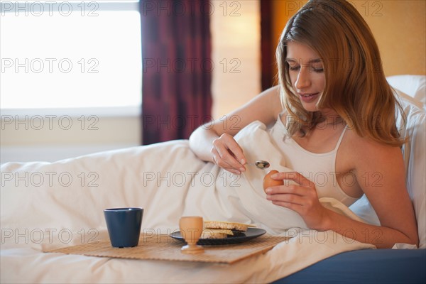 Young woman enjoying breakfast in bed. Photo : Mark de Leeuw