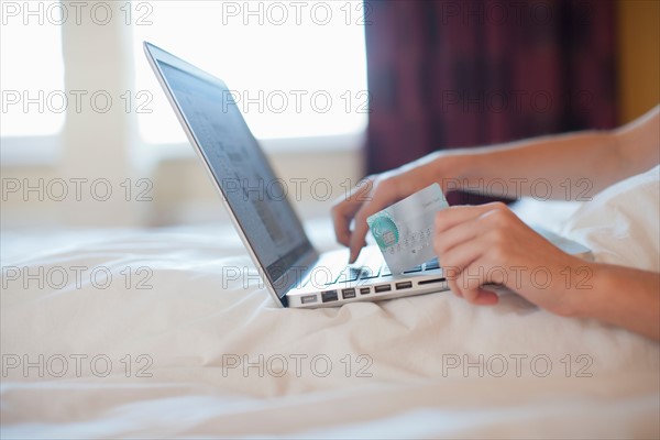 Young woman online shopping while in bed. Photo : Mark de Leeuw