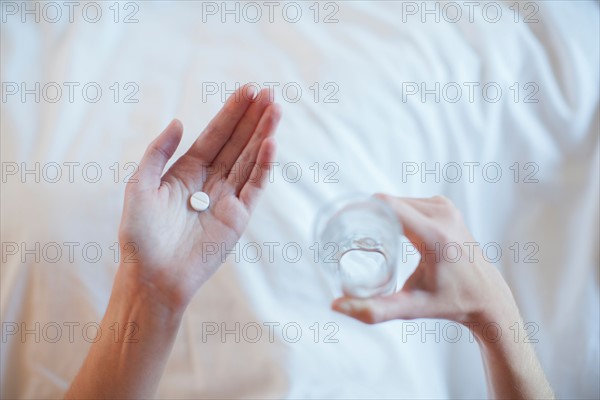 Young woman taking medicine while lying in bed . Photo : Mark de Leeuw