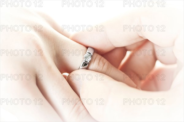 Close-up studio shot of man's hand putting engagement ring on female hand . Photo : Elena Elisseeva