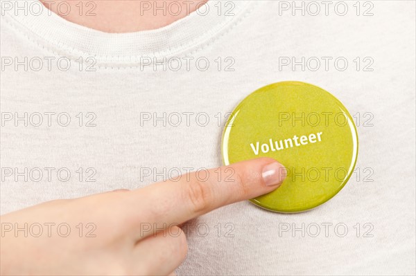 Close-up studio shot female hand pointing at yellow volunteer badge. Photo : Elena Elisseeva
