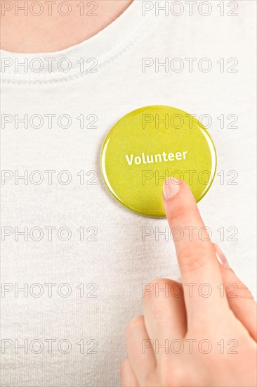 Close-up studio shot female hand pointing at yellow volunteer badge. Photo : Elena Elisseeva