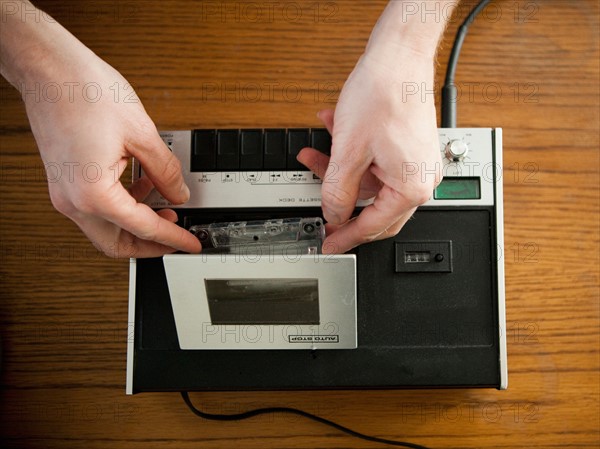 Close-up view of human hands putting tape into old-fashioned tape recorder. Photo : Jessica Peterson
