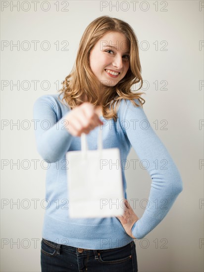 Indoor portrait young happy woman showing white present bag. Photo : Jessica Peterson