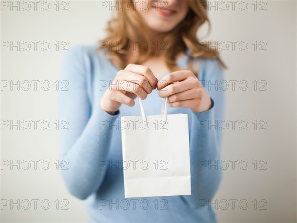 Indoor portrait young happy woman showing white present bag. Photo : Jessica Peterson