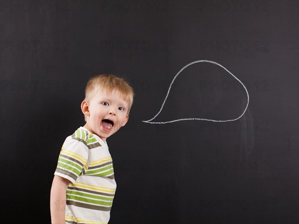 Studio portrait of happy toddler boy (2-3) with blank speech bubble written on blackboard. Photo : Jessica Peterson