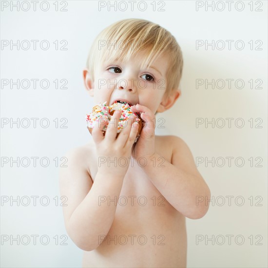 Studio portrait of cute toddler boy (2-3) eating doughnut. Photo : Jessica Peterson