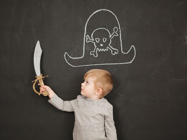Cute toddler boy (2-3) standing against blackboard posing as pirate. Photo : Jessica Peterson