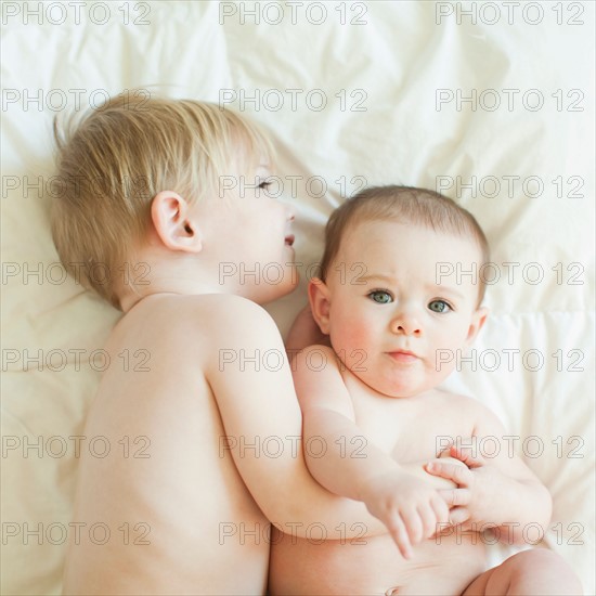 Toddler boy (2-3) lying in bed with baby sister (6-11 months). Photo : Jessica Peterson