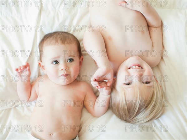 Toddler boy (2-3) lying in bed with baby sister (6-11 months). Photo : Jessica Peterson
