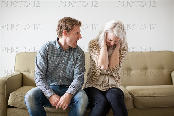 Young couple arguing while sitting on sofa. Photo : Jessica Peterson