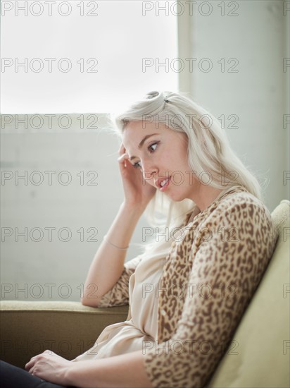 Thoughtful young woman sitting on sofa. Photo : Jessica Peterson