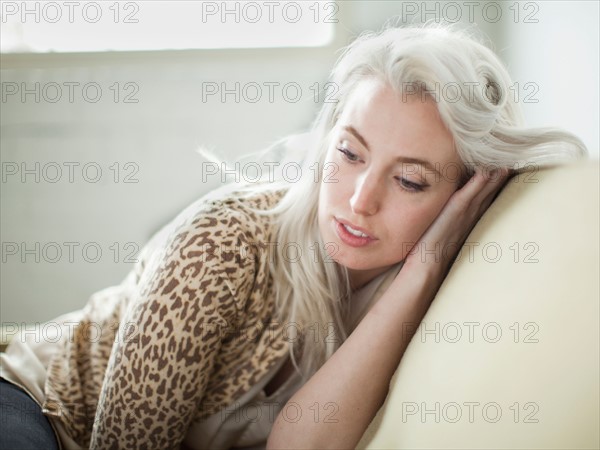 Thoughtful young woman sitting on sofa. Photo : Jessica Peterson