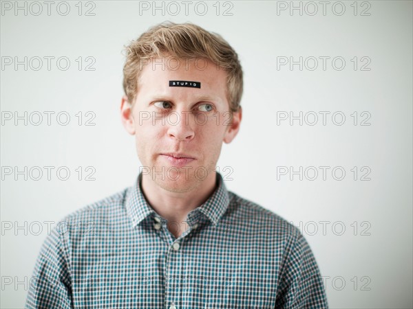 Studio shot of young man with black concept label on forehead. Photo : Jessica Peterson