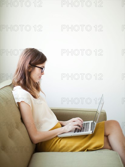 Young woman sitting on sofa with laptop. Photo : Jessica Peterson