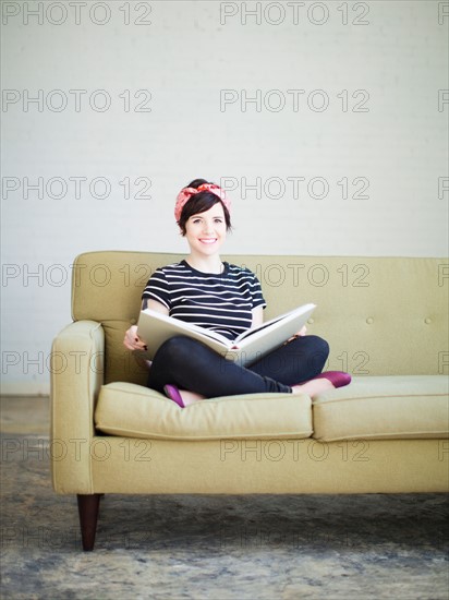 Young woman sitting on sofa with book. Photo : Jessica Peterson