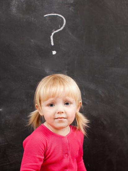 Portrait of baby girl (18-23 months) in front of blackboard. Photo : Jessica Peterson