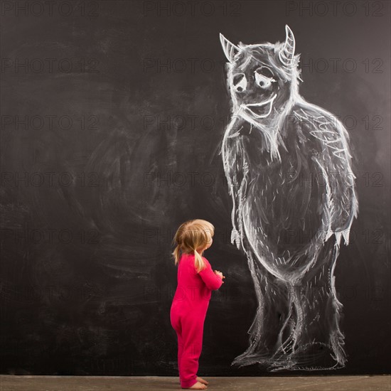 Portrait of baby girl (18-23 months) in front of huge monster drawn on blackboard. Photo : Jessica Peterson
