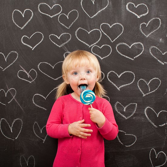 Portrait of baby girl (18-23 months) eating lollipop. Photo : Jessica Peterson