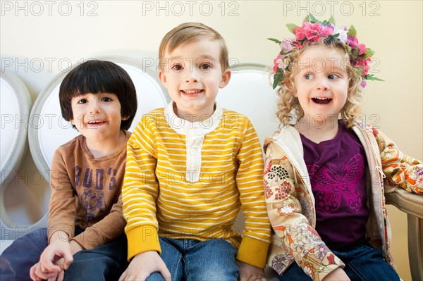 Studio Shot portrait of three children (4-5, 6-7) sitting side by side. Photo : Jessica Peterson