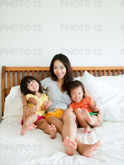 Portrait of mother with daughters (2-3, 4-5) sitting on bed. Photo : Jessica Peterson