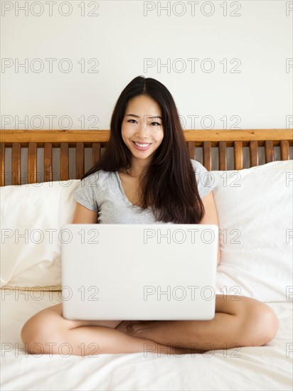 Young woman sitting on bed, using laptop. Photo : Jessica Peterson