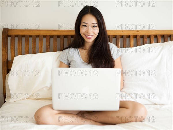 Young woman sitting on bed, using laptop. Photo : Jessica Peterson