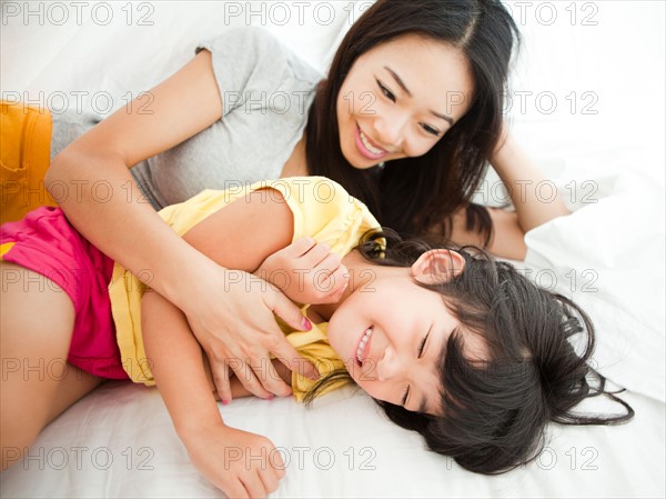 Mother with daughter lying down in bed, tickling (4-5). Photo : Jessica Peterson