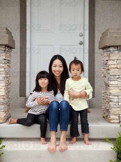 Portrait of mother sitting on doorsteps with two daughters (2-3, 4-5). Photo : Jessica Peterson