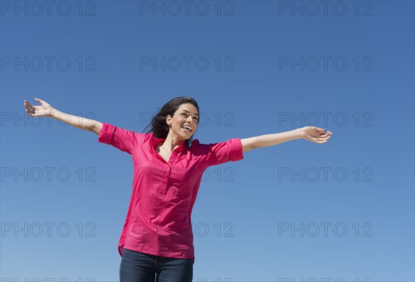 Young woman outstretching arms against blue sky.