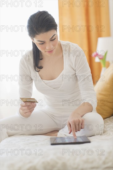 Young woman in bedroom using tablet pc for online shopping.