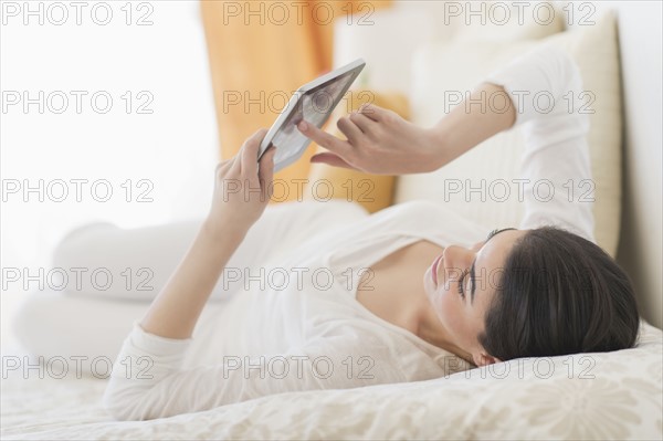 Young woman lying on bed using tablet pc.