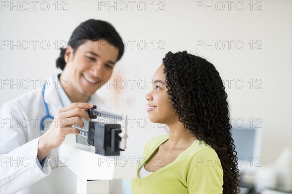 Doctor weighing female patient (10-11).