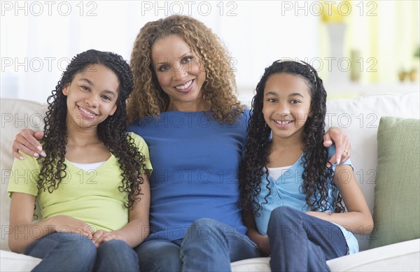 Portrait of mother with daughters (10-13) sitting on sofa.